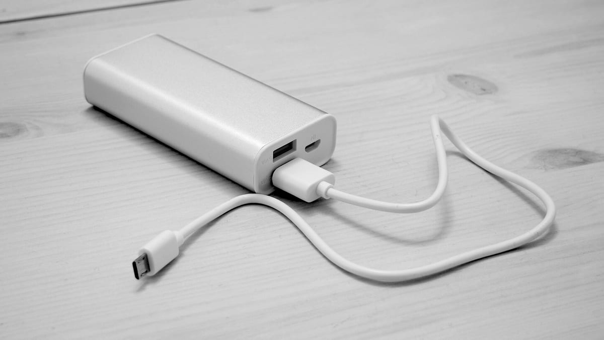 Một viên pin sạc dự phòng vỏ nhôm bạc đặt trên mặt gỗ trắng, cắm sẵn dây cáp micro USB